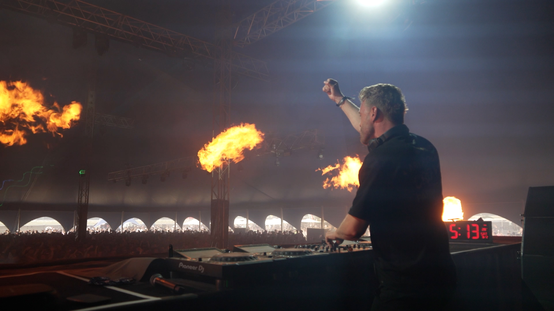 View from on the stage with a DJ fist pumping and pyrotechnics in the shot